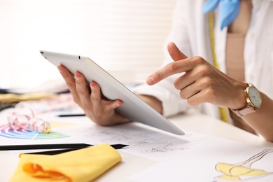 Fashion designer with tablet working at table in workshop, closeup