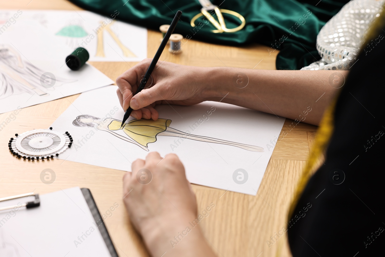 Photo of Fashion designer drawing sketch of beautiful dress at wooden table, closeup