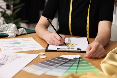 Photo of Fashion designer drawing sketch of beautiful dress at wooden table, closeup