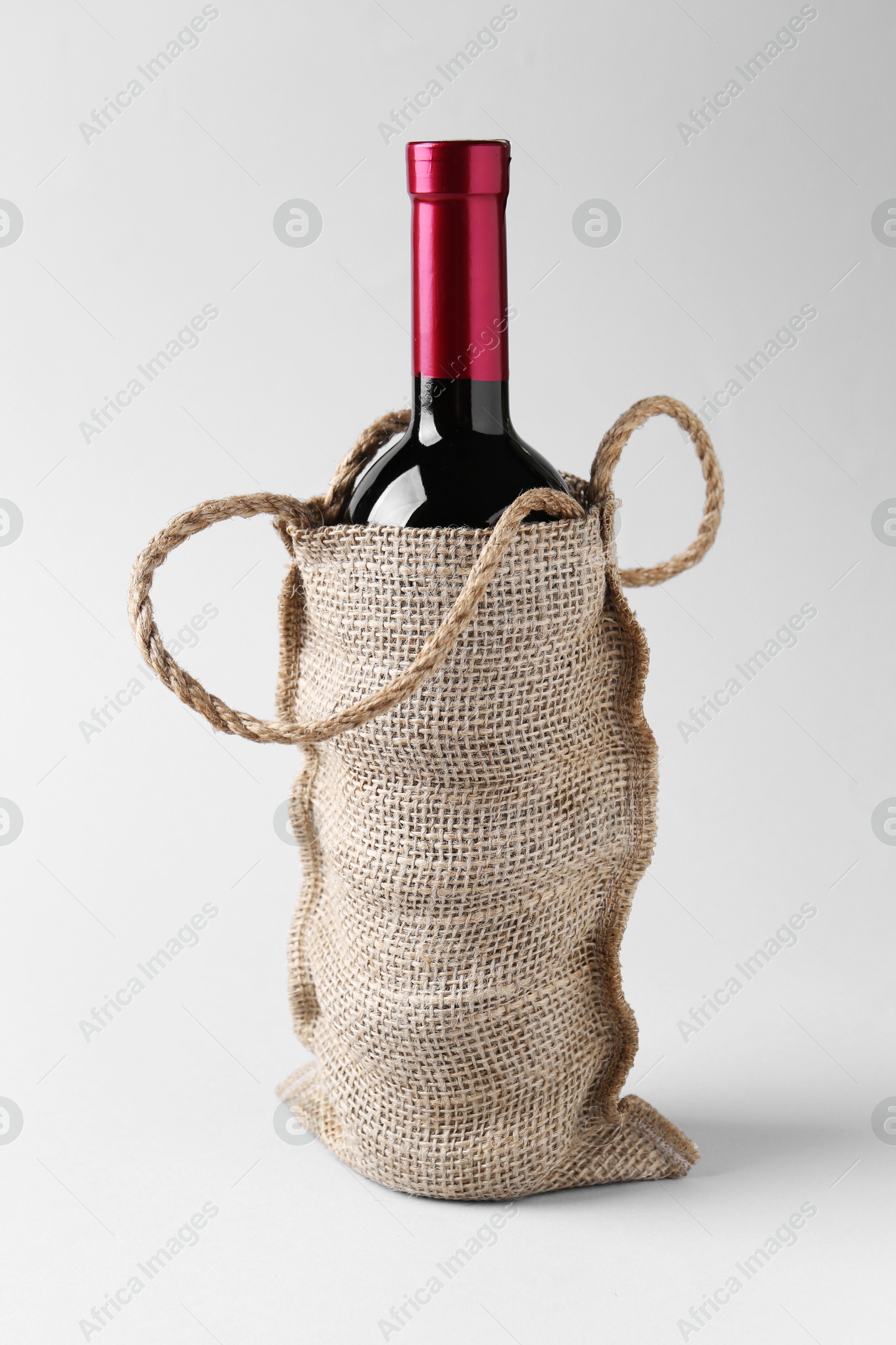 Photo of Wine bottle in burlap bag on light grey background