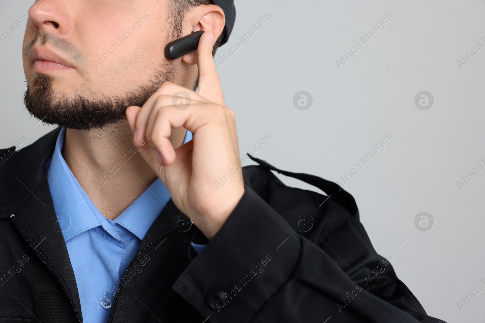 Photo of Security guard in uniform with earpiece on grey background, closeup