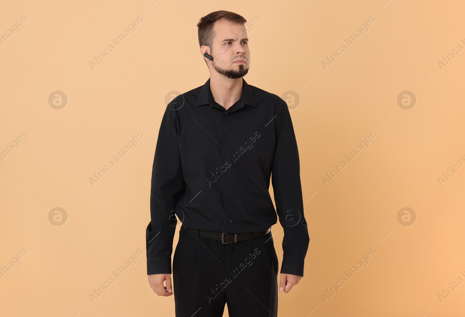 Photo of Young bodyguard with earpiece on beige background