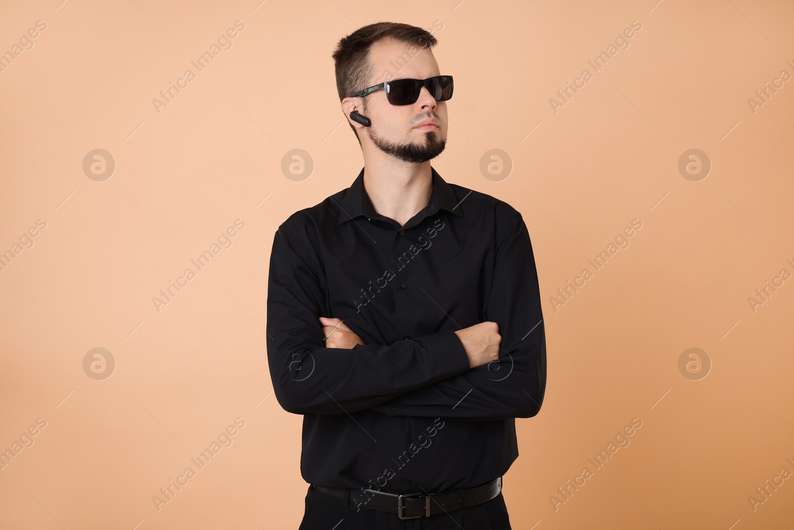 Photo of Young bodyguard in sunglasses and earpiece on beige background