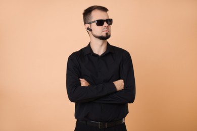 Photo of Young bodyguard in sunglasses and earpiece on beige background