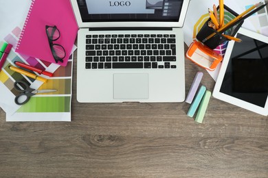 Fashion designer`s workplace with laptop, tablet and different stationery on wooden table, flat lay