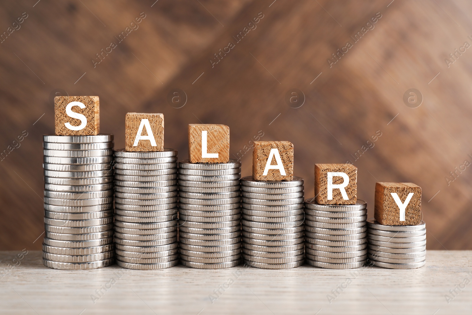 Photo of Stacked coins and cubes with word Salary on light wooden table, closeup