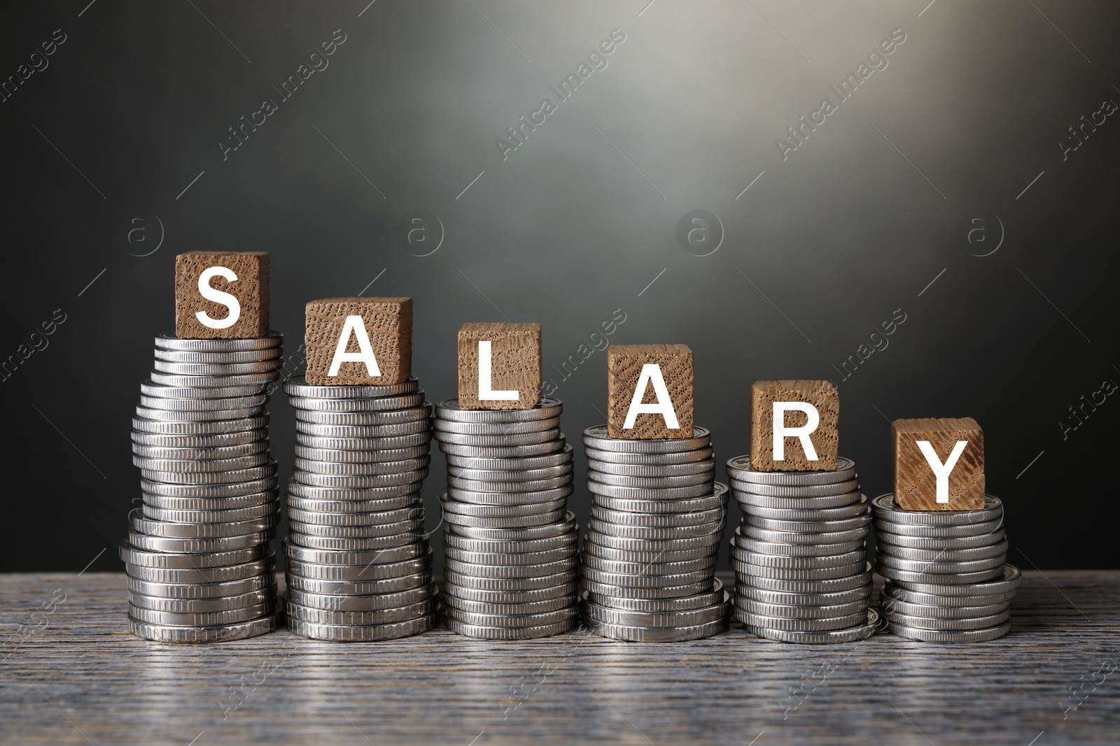 Photo of Stacked coins and cubes with word Salary on wooden table, closeup