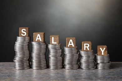 Photo of Stacked coins and cubes with word Salary on wooden table, closeup