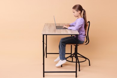 Photo of Girl with correct posture using laptop at wooden desk on beige background