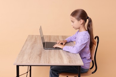 Photo of Girl with correct posture using laptop at wooden desk on beige background