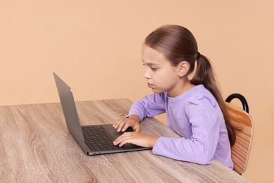 Girl with incorrect posture using laptop at wooden desk on beige background