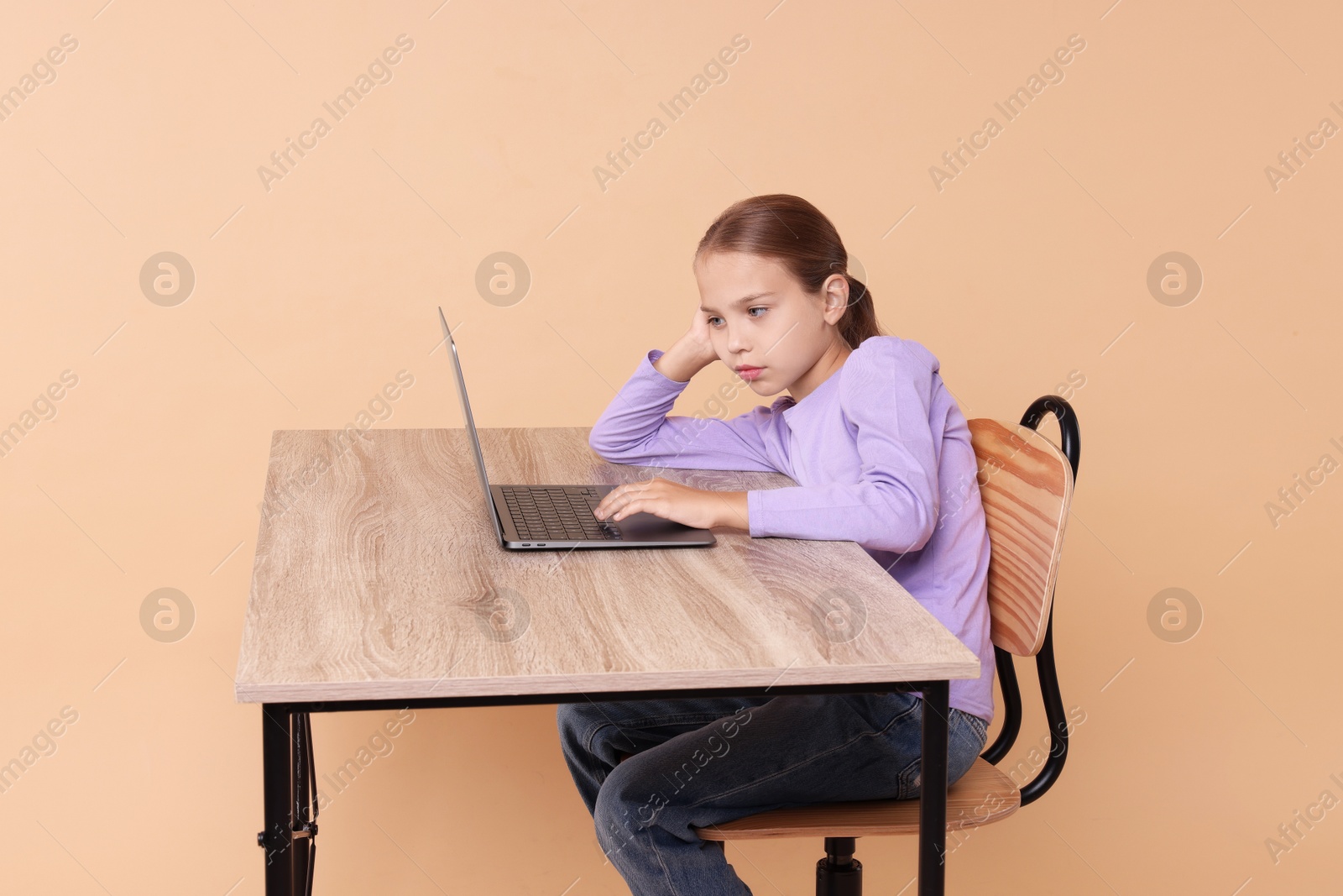 Photo of Girl with incorrect posture using laptop at wooden desk on beige background