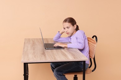 Photo of Girl with incorrect posture using laptop at wooden desk on beige background