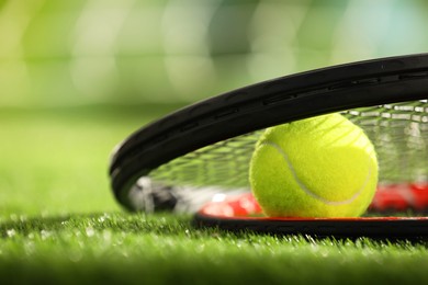 Photo of Tennis racket and ball on green artificial grass, closeup