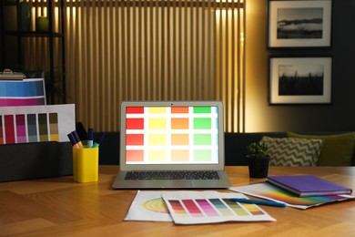 Designer's workplace with laptop, stationery and palettes on wooden table indoors