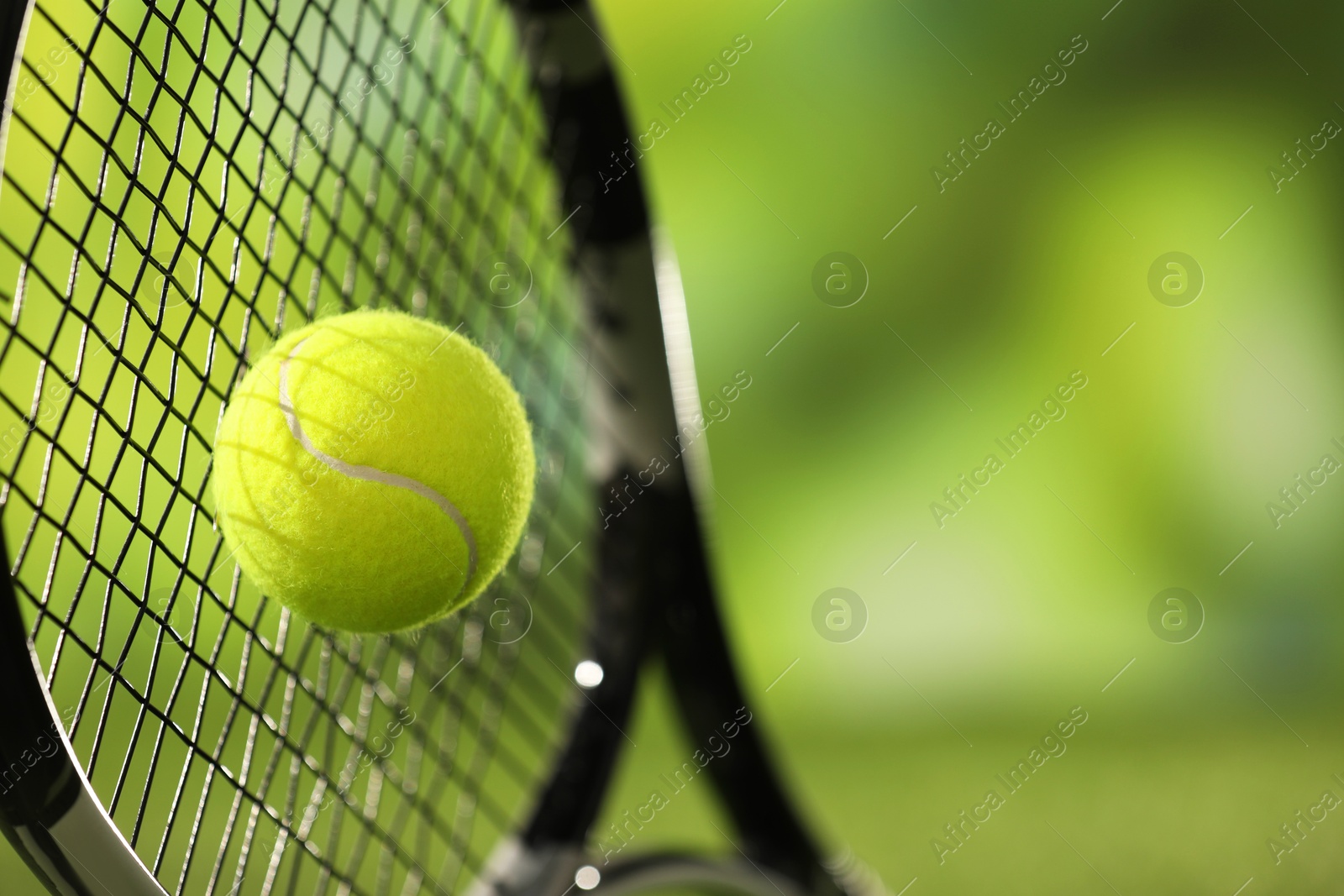 Photo of Tennis racket with ball against blurred green background, closeup. Space for text