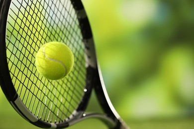 Photo of Tennis racket with ball against blurred green background, closeup. Space for text