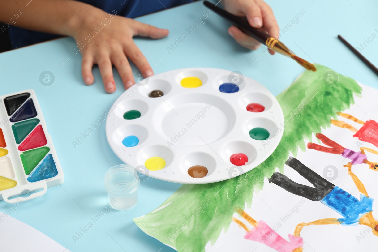 Photo of Boy with brush, palette, paints and picture at light blue table, closeup