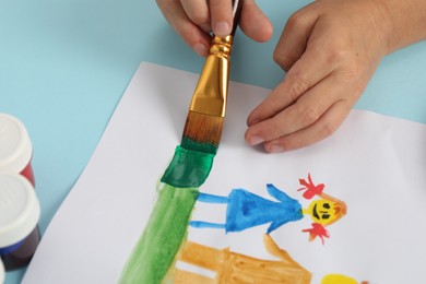 Photo of Boy drawing picture with paint at light blue table, closeup