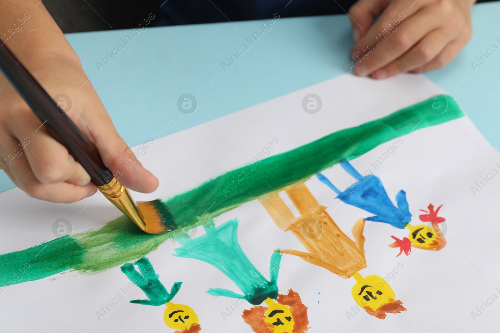 Photo of Boy drawing his family with paint at light blue table, closeup