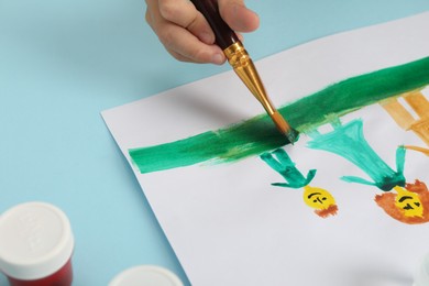 Photo of Boy drawing his family with paint at light blue table, closeup