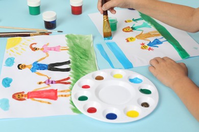 Photo of Boy drawing his family with paint at light blue table, closeup