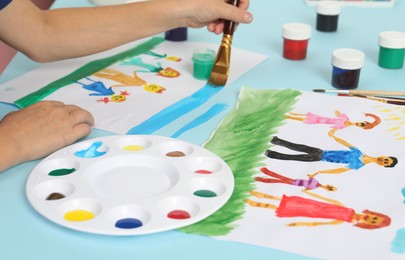 Photo of Boy drawing his family with paint at light blue table, closeup