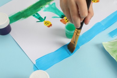 Photo of Boy drawing his family with paint at light blue table, closeup