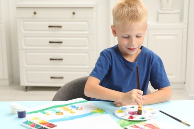 Photo of Little boy drawing picture with paint at table indoors. Space for text