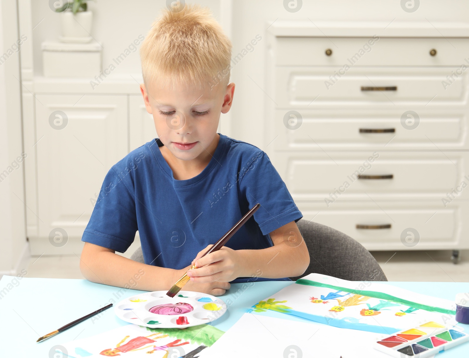 Photo of Little boy drawing picture with paint at table indoors