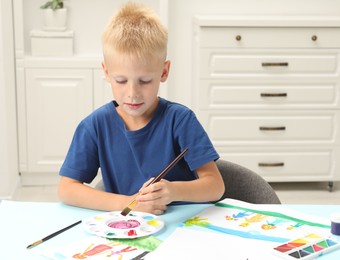 Photo of Little boy drawing picture with paint at table indoors