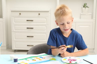 Little boy drawing picture with paint at table indoors. Space for text