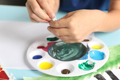 Photo of Boy at light blue table with picture, palette and paint, closeup