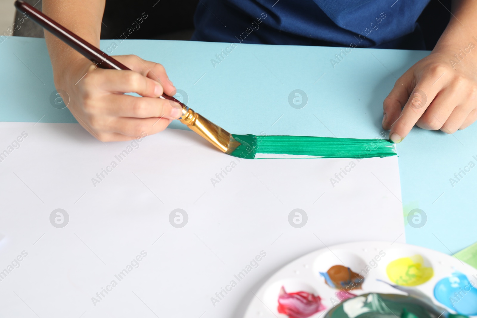 Photo of Boy drawing picture with paint at light blue table, closeup