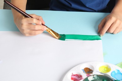 Photo of Boy drawing picture with paint at light blue table, closeup