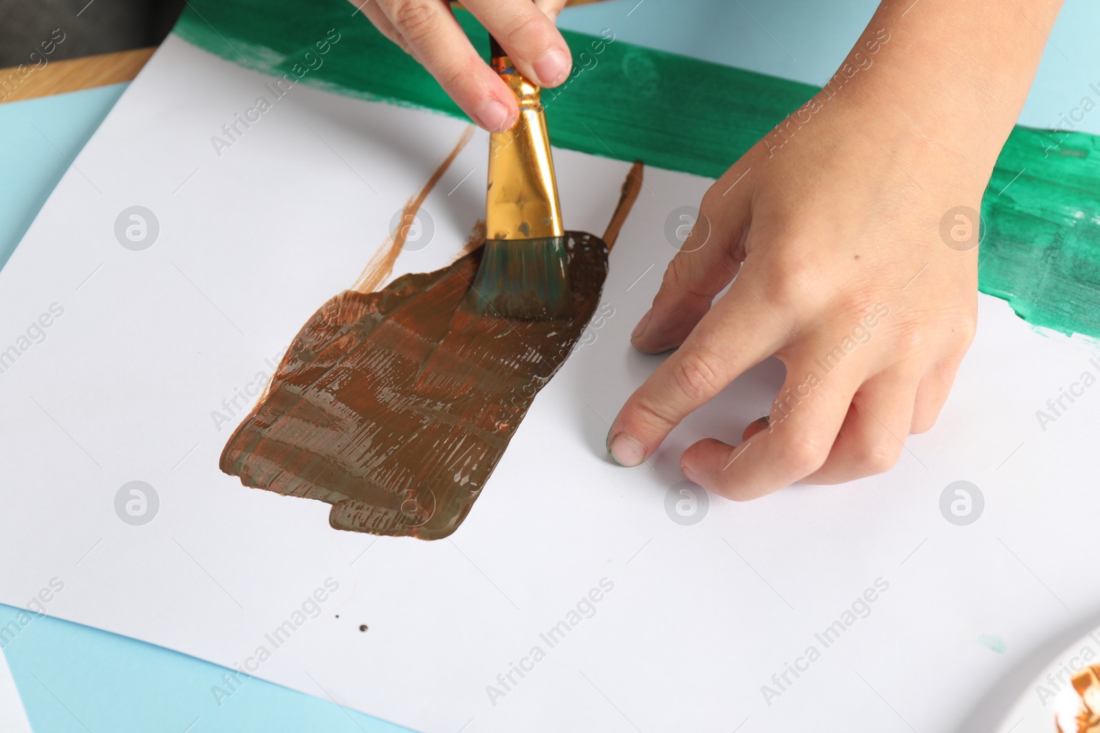 Photo of Boy drawing picture with paint at light blue table, closeup