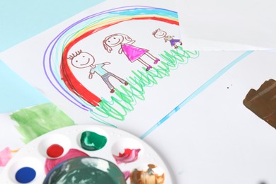 Photo of Child`s drawings and palette with paints on light blue table, closeup