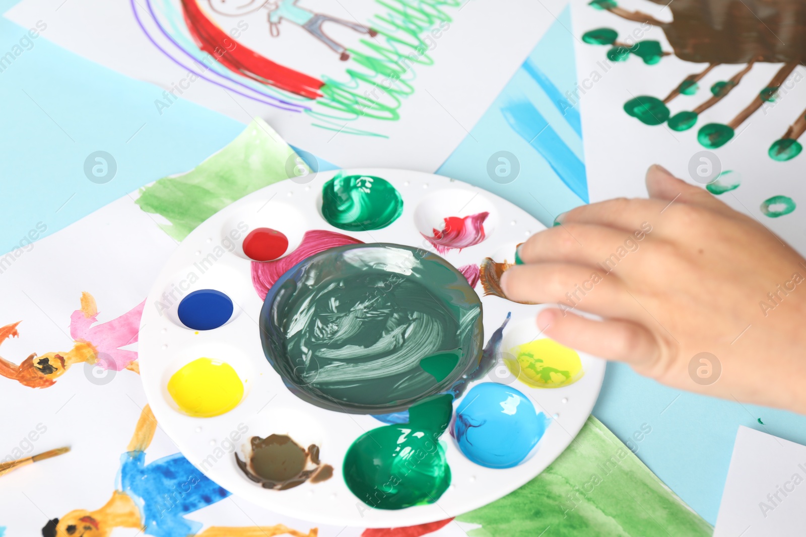 Photo of Boy drawing picture with paint at light blue table, closeup