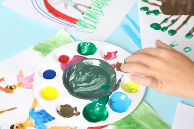 Photo of Boy drawing picture with paint at light blue table, closeup