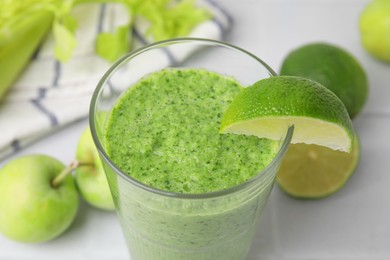 Photo of Tasty green smoothie in glass with lime and apples on light table, closeup