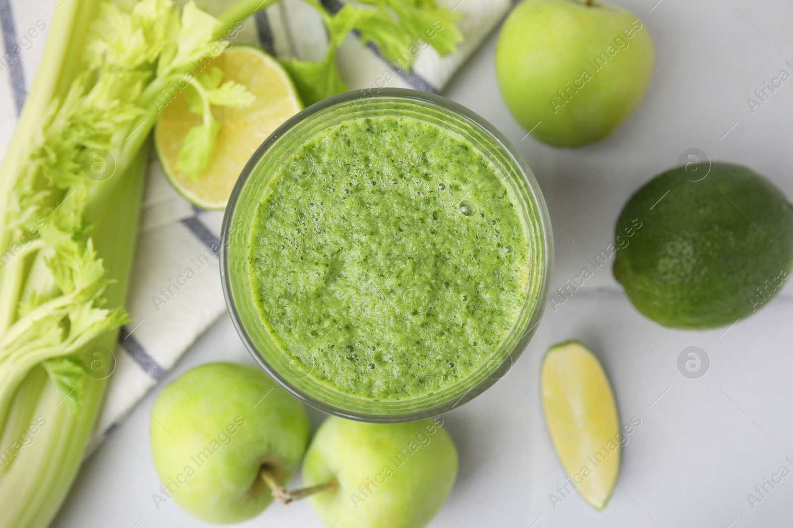 Photo of Tasty green smoothie in glass, lime, celery and apples on white tiled table, flat lay