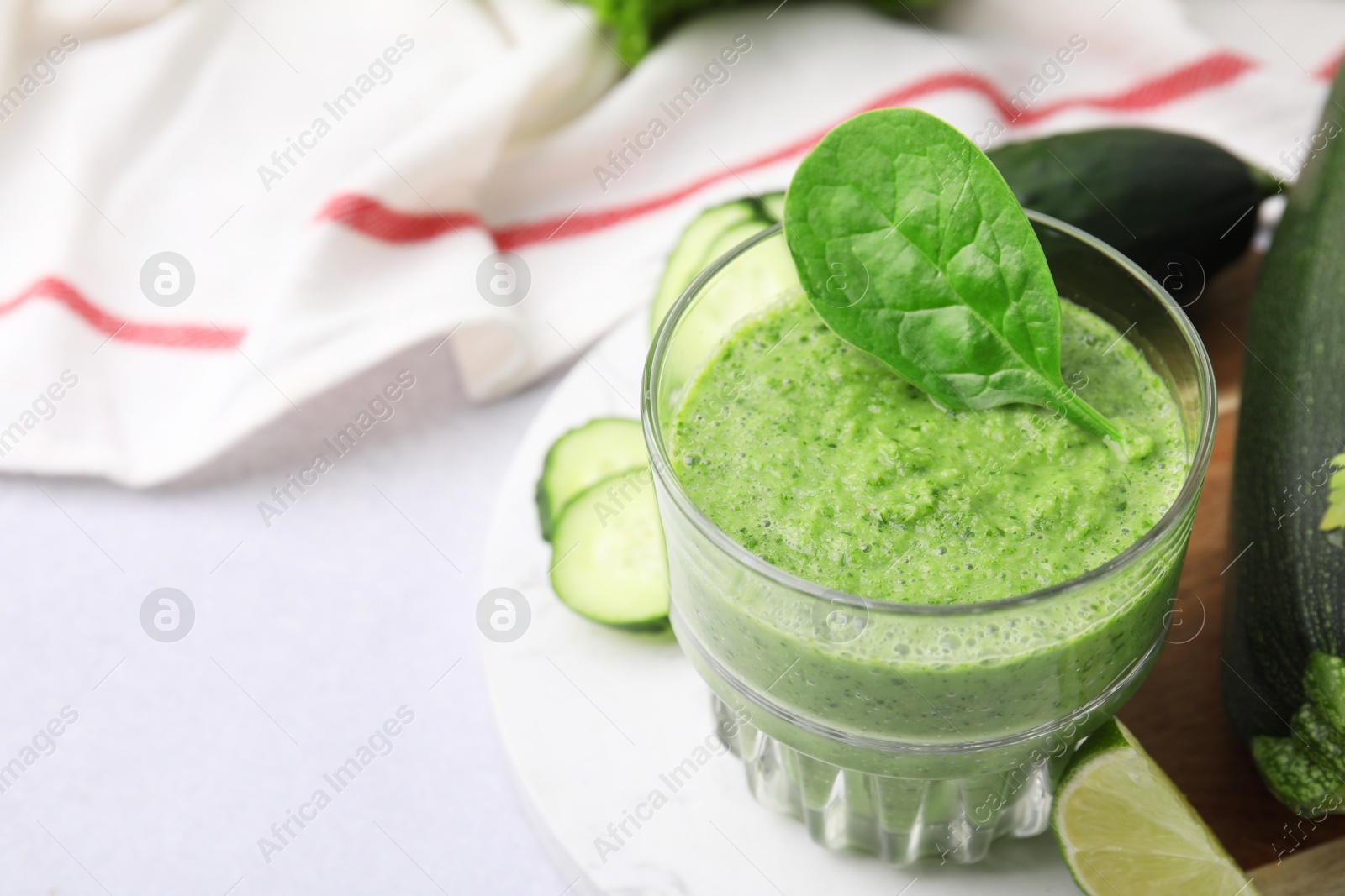 Photo of Tasty green smoothie in glass, lime and vegetables on light table, closeup. Space for text