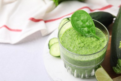 Photo of Tasty green smoothie in glass, lime and vegetables on light table, closeup. Space for text