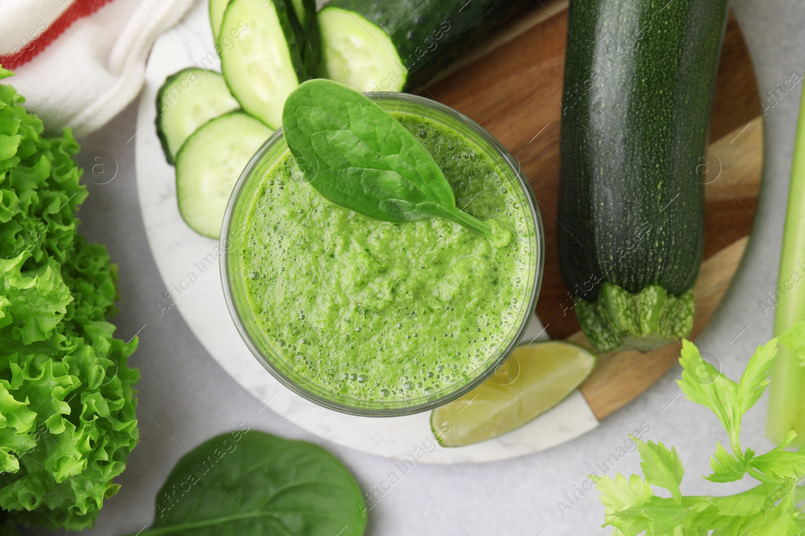 Photo of Tasty green smoothie in glass, lime and vegetables on light table, flat lay