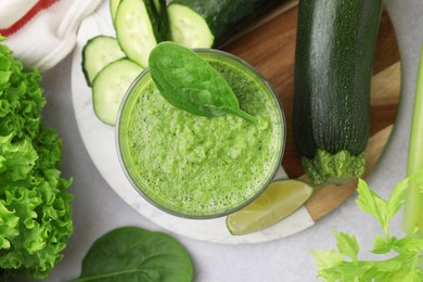 Photo of Tasty green smoothie in glass, lime and vegetables on light table, flat lay