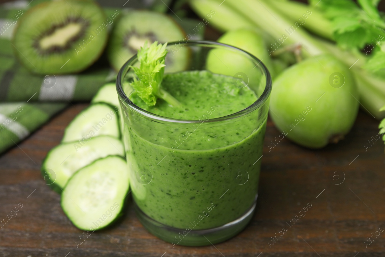 Photo of Tasty green smoothie in glass and cut cucumber on wooden table, closeup