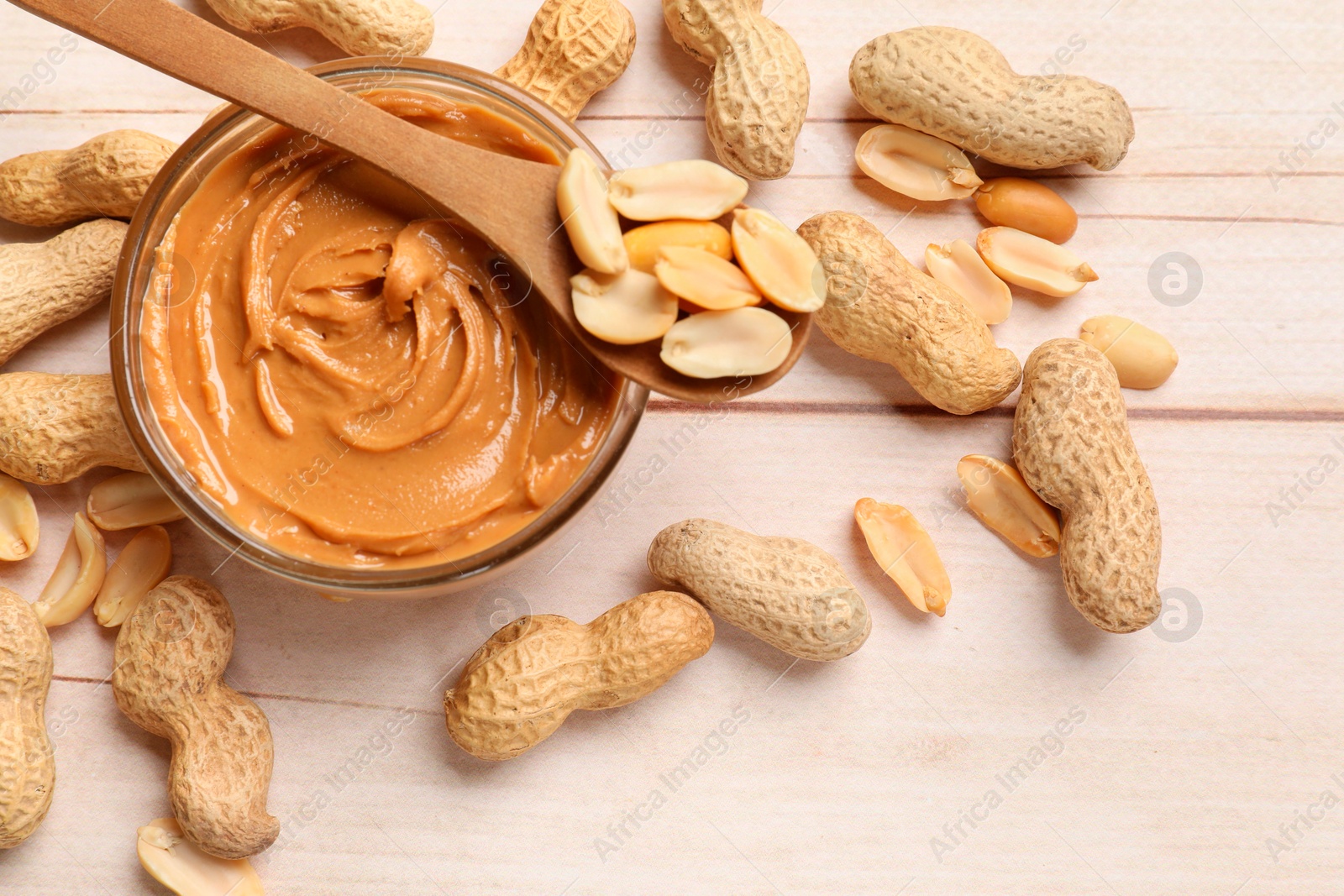 Photo of Tasty peanut butter in bowl and nuts on wooden table, flat lay