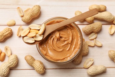 Photo of Tasty peanut butter in bowl and nuts on wooden table, flat lay