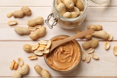 Photo of Tasty peanut butter in bowl, nuts, jar and spoon on wooden table, flat lay