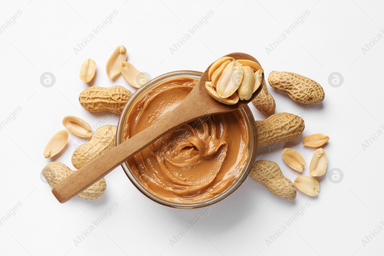 Photo of Tasty peanut butter in bowl and spoon with groundnuts on white table, flat lay